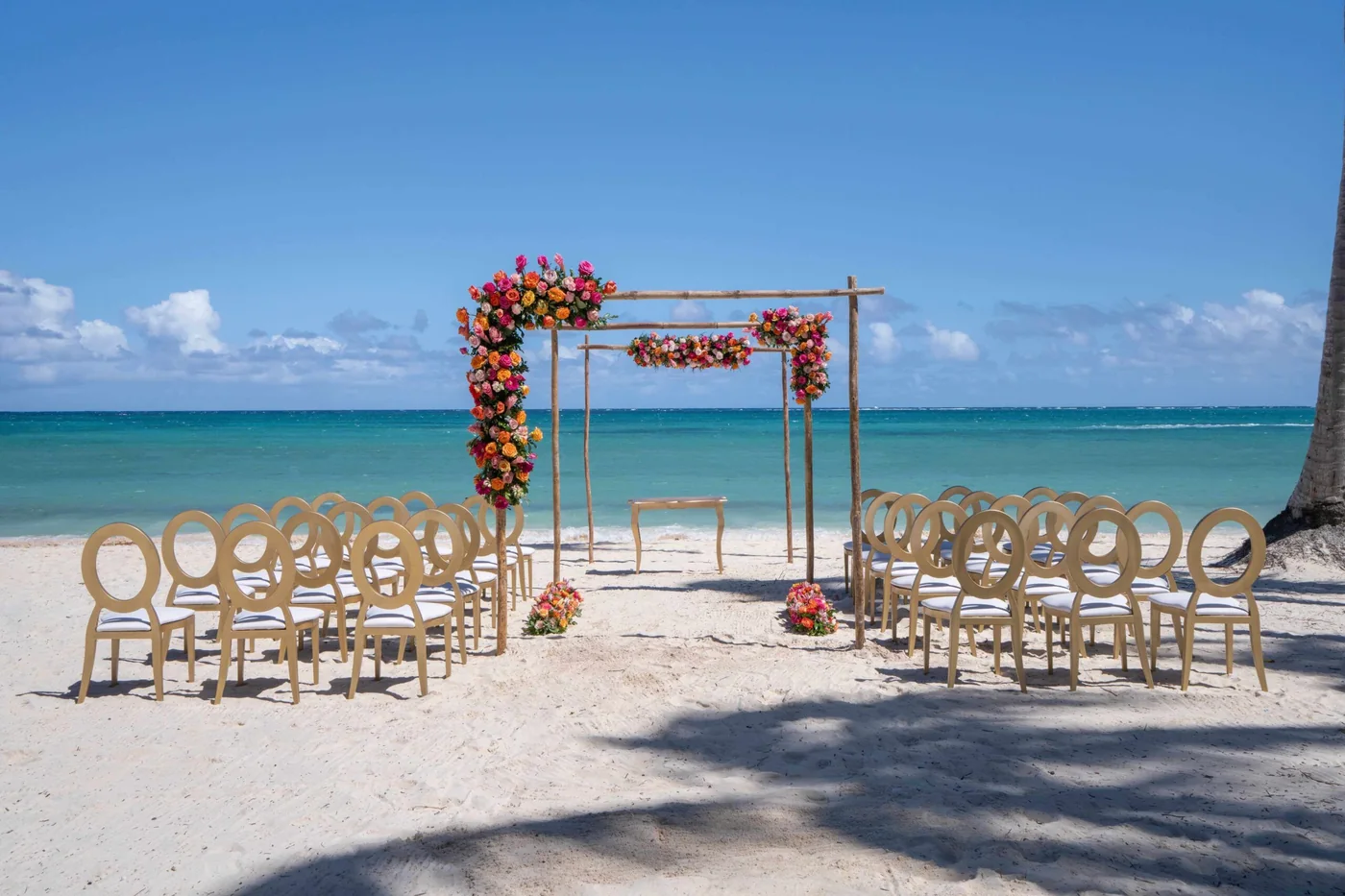 A bamboo ceremony structure on a Caribbean beach at the water's edge, chairs set on the sand, before decoration